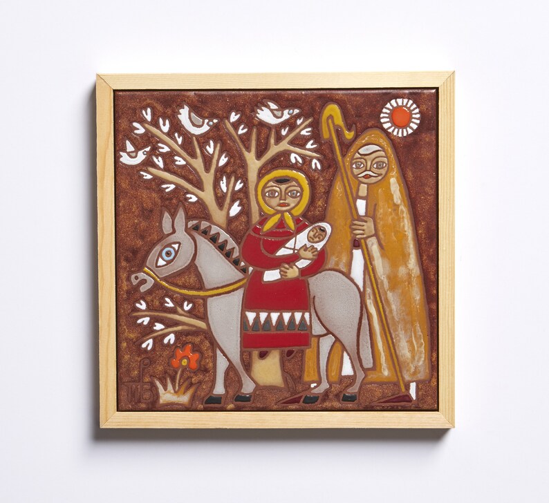 May include: A framed ceramic tile depicting a religious scene. The artwork features a woman holding a baby on a donkey, accompanied by a man with a staff. The color palette includes brown, red, yellow, and white, with a tree and birds in the background.