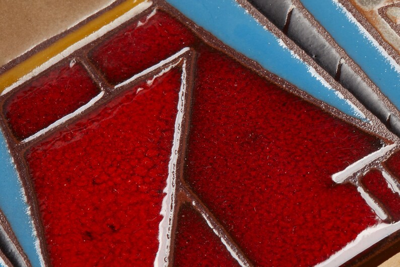 May include: Close-up of a red, blue, and white ceramic tile with a geometric pattern. The tile has a textured surface and is made of glazed ceramic.