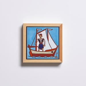 Pode incluir: Azulejo emoldurado com uma ilustração náutica. A obra retrata uma pessoa em pé num veleiro com uma vela branca contra um céu azul. O barco é vermelho e creme, e a moldura é de madeira natural.