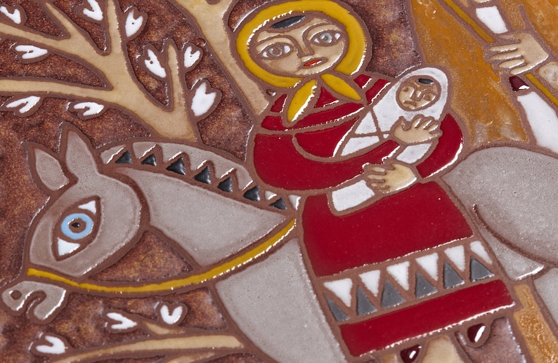 May include: A ceramic tile featuring a stylized illustration of a woman in a red dress and yellow head covering holding a baby wrapped in white. The woman is riding a gray horse with a yellow bridle. The background is brown with white leaf shapes.