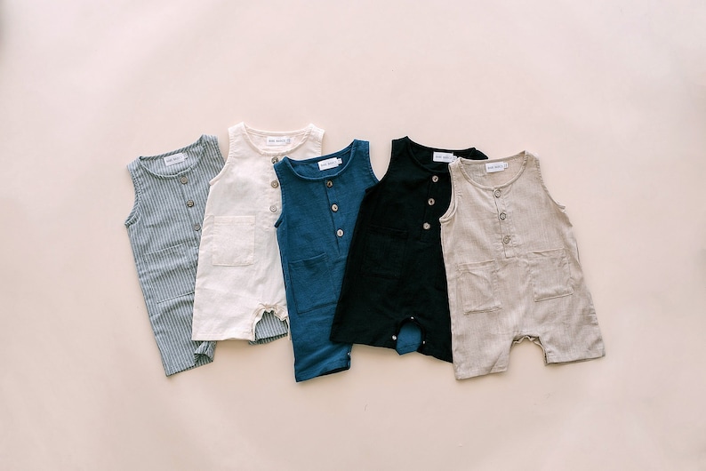 May include: Five sleeveless baby onesies in different colors and patterns. The onesies are made of a soft, lightweight fabric and have a button closure at the front. The onesies are arranged in a row on a light beige background.