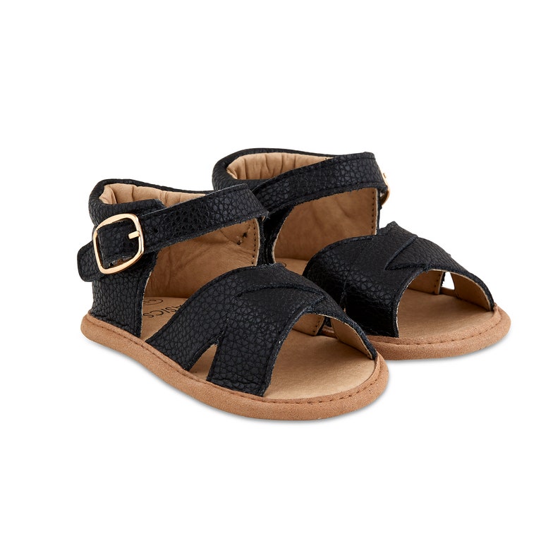May include: Black leather baby sandals with a buckle fastening and a brown sole.