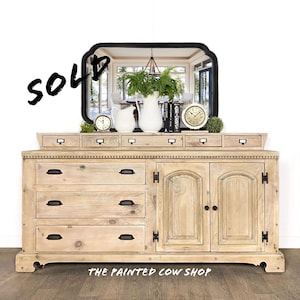 May include: A light wood dresser with six drawers and two doors. The dresser has a top shelf with four small drawers. The dresser is decorated with black hardware. The dresser is sold. The Painted Cow Shop is written on the bottom of the image.
