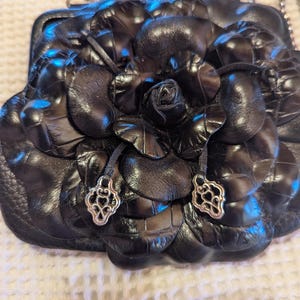 K&ouml;nnte beinhalten: Schwarze Lederhandtasche in Form einer Rose mit silbernen Akzenten. Die Tasche hat einen Kettenriemen.