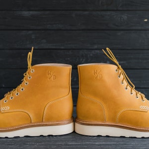 Puede incluir: Un par de botas de cuero amarillo con suelas y cordones blancos. Las botas tienen un logotipo en el lateral que dice "W/B".