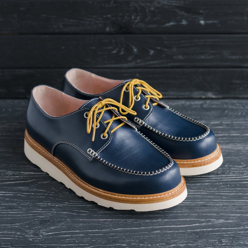 May include: A pair of blue leather shoes with yellow laces. The shoes have a white sole and a brown leather trim around the top.