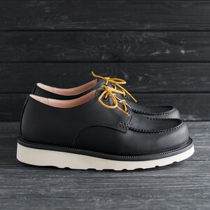 Peut inclure: Chaussures en cuir noir &agrave; lacets avec une semelle blanche et des lacets jaunes. Les chaussures ont un style d&eacute;contract&eacute; et confortable.