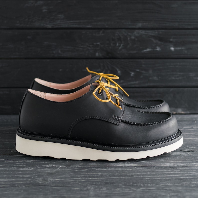Peut inclure: Chaussures en cuir noir &agrave; lacets avec une semelle blanche et des lacets jaunes. Les chaussures ont un style d&eacute;contract&eacute; et confortable.