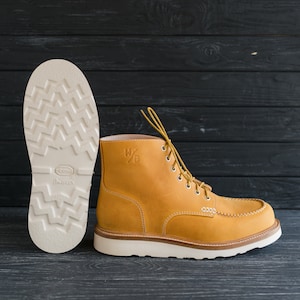Puede incluir: Un par de botas de cuero amarillo con cordones blancos y suela blanca. Las botas tienen un ribete de cuero marr&oacute;n alrededor de la parte superior y una suela de goma blanca. Las botas tienen un logotipo en el lateral que dice "W/D".
