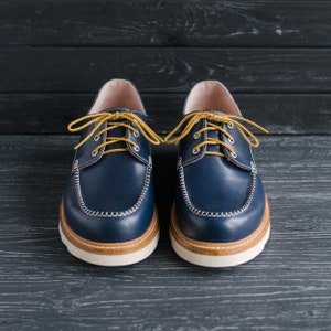 May include: A pair of blue leather boat shoes with yellow laces. The shoes have white stitching around the edges and a white sole.