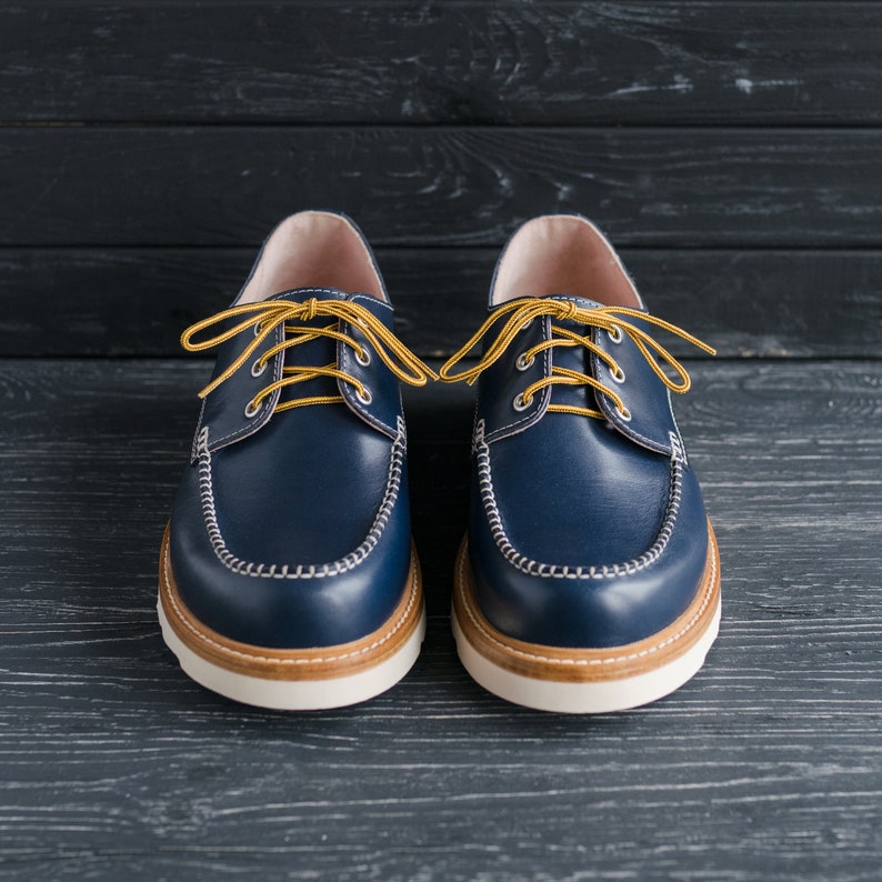 May include: A pair of blue leather boat shoes with yellow laces. The shoes have white stitching around the edges and a white sole.