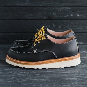 May include: A pair of black leather lace-up shoes with a white sole and yellow laces. The shoes have a casual, comfortable style.
