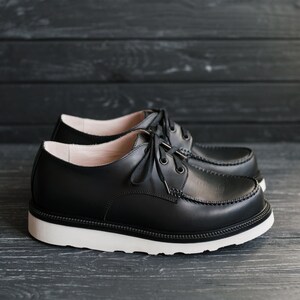 Peut inclure: Une paire de chaussures en cuir noir &agrave; lacets avec des semelles blanches. Les chaussures ont un style d&eacute;contract&eacute; et sont faites d'un mat&eacute;riau durable.