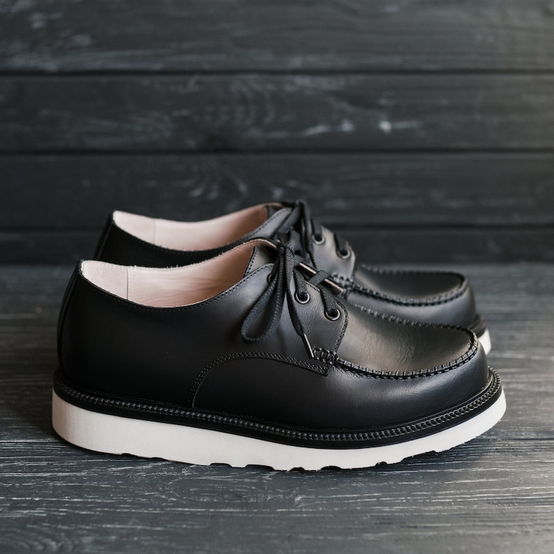 Peut inclure: Une paire de chaussures en cuir noir &agrave; lacets avec des semelles blanches. Les chaussures ont un style d&eacute;contract&eacute; et sont faites d'un mat&eacute;riau durable.