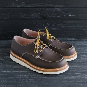 May include: Two pairs of brown leather shoes with yellow laces. The shoes have a white sole and a brown leather upper.
