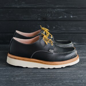 May include: A pair of black leather shoes with yellow laces. The shoes have a white sole and a brown leather trim around the edge.