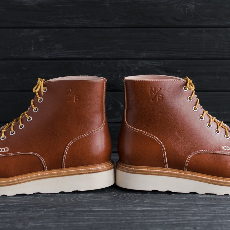 May include: A pair of brown leather boots with white soles and laces. The boots have a logo on the side that says "N/B".