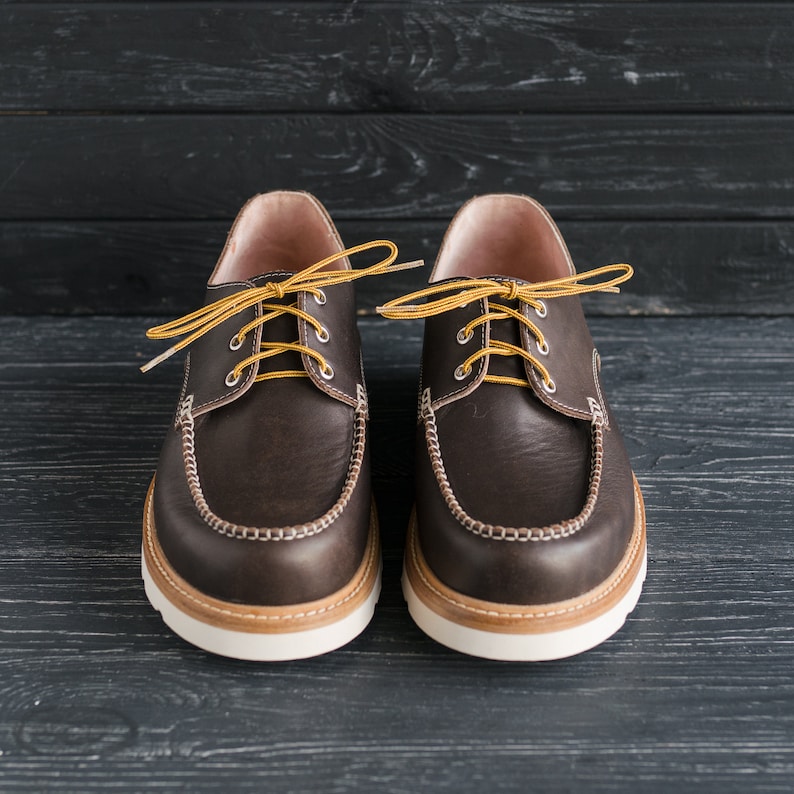 May include: A pair of brown leather boat shoes with yellow laces. The shoes have a white rubber sole and a brown leather upper.