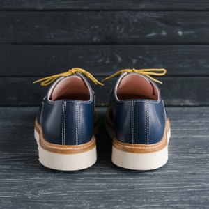 May include: A pair of blue leather shoes with yellow laces. The shoes have a white sole and a brown leather trim around the top.