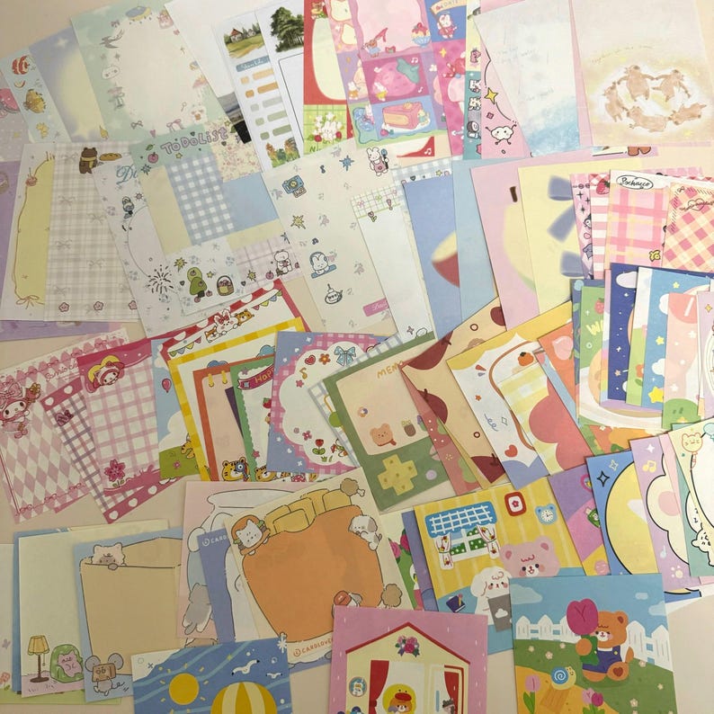 May include: A collection of colorful stationery items, including notepaper, cards, and envelopes. The designs feature various cute illustrations, such as bears, cakes, and other whimsical elements. The color palette includes pastels and bright hues, creating a playful aesthetic.