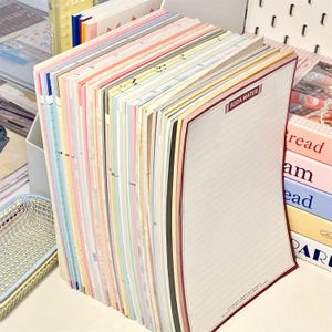 Peut inclure: Une pile de blocs de papier lignés colorés avec une bordure rouge et le texte "SODA WATER" sur le bloc du dessus.