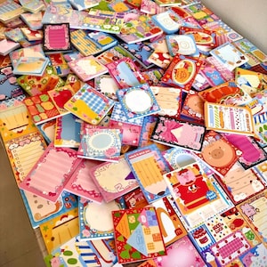 May include: A large assortment of colorful, decorative notepads with various designs, including pigs, food, and patterns. The notepads are in various shapes and sizes, with blank spaces for writing. The image is a top-down view of the notepads.