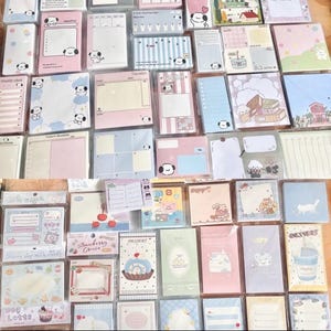May include: A collection of various stationery items, including notepads and sticky notes, in a variety of pastel colors. Many feature cute cartoon dog illustrations. Some items have text, such as "Strawberry Cruise" and "Dessert".