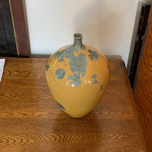 May include: A yellow ceramic vase with a round body and a narrow neck. The vase is decorated with blue and green floral patterns.