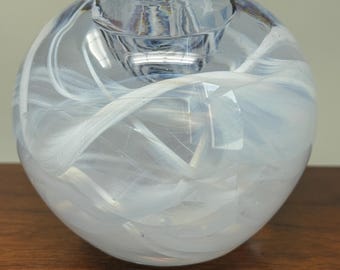 May include: A spherical clear glass candle holder featuring swirling white opaque patterns throughout the body. The piece has a circular opening at the top designed to hold a candle, with a smooth, polished surface and a rounded, globe-like shape.
