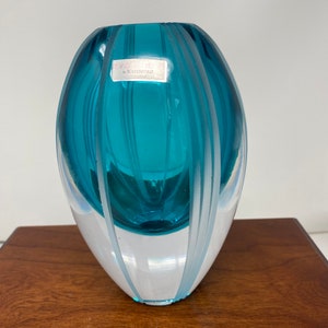 May include: A teal blue glass vase with white stripes. The vase is oval shaped and has a label that reads "EVOLUTION by WATERFORD."