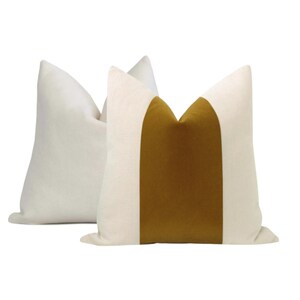May include: Two decorative throw pillows with a white linen fabric and a mustard yellow velvet accent. The pillows are arranged side by side.