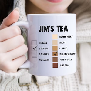 May include: White ceramic mug with the text "JIM'S TEA" and a checklist for different tea preferences. The options include "1 sugar", "2 sugars", "3 sugars", "no sugar", "really milky", "milky", "classic", "builder's brew", "just a drop", and "just tea".