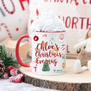 May include: White ceramic mug with a red handle. The mug features a Christmas Eve design with the text "Chloe's Christmas Eve mug" and various Christmas illustrations. The mug is filled with whipped cream.