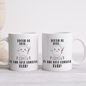 May include: Two white ceramic mugs featuring a tooth graphic and the text "Tooth be told... Sonia is the best dentist ever!"