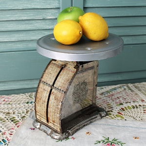 May include: A vintage silver and white kitchen scale with a round platform and a dial face. Three green and yellow fruits are on the platform.