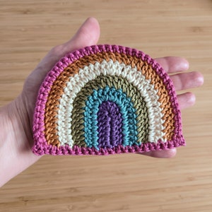 May include: A crocheted rainbow made with different colored yarn. The rainbow is pink, orange, cream, green, blue, purple, and pink again.