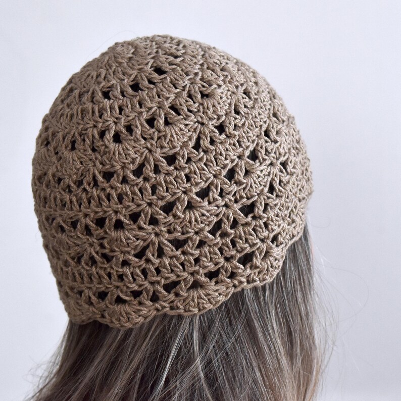Puede incluir: Un gorro de ganchillo de color marr&oacute;n claro con un intrincado patr&oacute;n de puntos en forma de abanico. El gorro est&aacute; construido con un dise&ntilde;o ligero de tejido abierto que crea una apariencia texturizada y festoneada en toda la superficie.