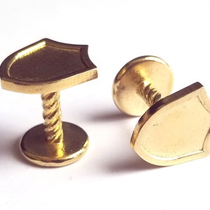 May include: A pair of gold-toned cufflinks with a shield design. Each cufflink has a twisted post and a round base.