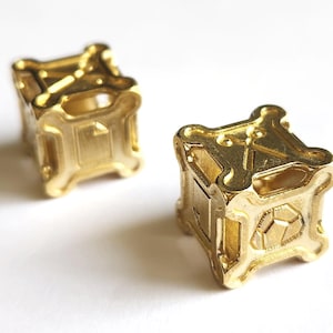 May include: Two gold metal dice with intricate designs on each face. The dice are made of a solid metal and have a shiny finish.