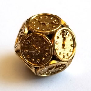 May include: A gold-colored, multi-sided die with clock faces on each side. The die is made of metal and has a textured surface.