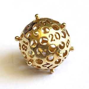 May include: A gold-colored, spherical dice with numbers 1 through 20 etched into the surface. The dice has a hollow, open design with small, round protrusions at each point.