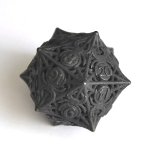 May include: A black, intricately designed 20-sided die with numbers 1-20 on each face. The die is made of a textured material and has a geometric shape.