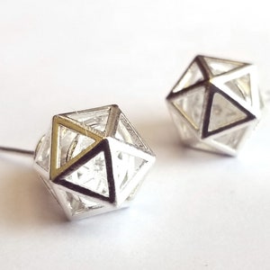 May include: Two silver-colored geometric stud earrings. Each earring features a hollow, three-dimensional shape with triangular and square facets. The earrings are displayed on a white background.