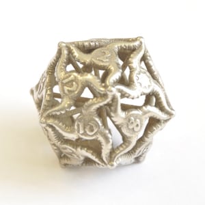 May include: A silver metal d20 dice with a unique, intricate design. The numbers 1 through 20 are visible on the faces of the dice.