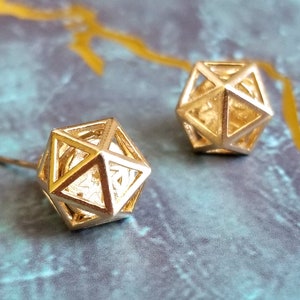 May include: A pair of gold geometric earrings with a cage-like design. The earrings are made of metal and have a shiny finish.