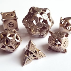 May include: A set of six silver metal dice with different numbers of sides. The dice are all intricately designed with various patterns and textures.