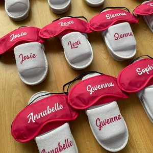 May include: A set of white slippers with pink eye masks. Each slipper has a different name embroidered on it, including Rosie, Harper, Charlotte, Josie, Lexi, Sienna, Gwenna, and Annabelle.