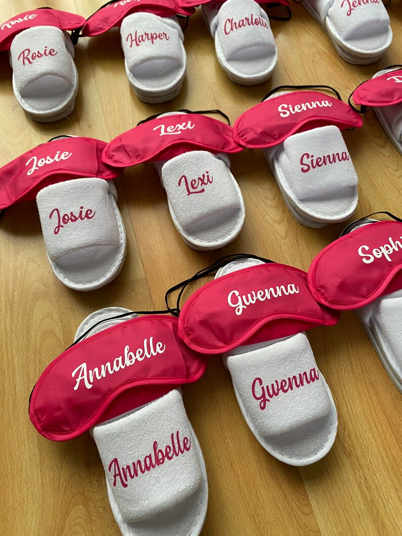 May include: A set of white slippers with pink eye masks. Each slipper has a different name embroidered on it, including Rosie, Harper, Charlotte, Josie, Lexi, Sienna, Gwenna, and Annabelle.