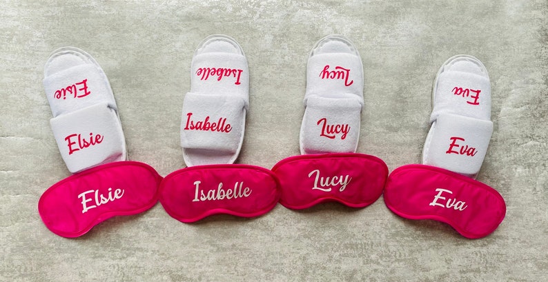 May include: Four pairs of white slippers with pink eye masks. Each pair of slippers and eye mask has a name embroidered on them: Elsie, Isabelle, Lucy, and Eva.