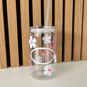 May include: A clear plastic tumbler with a white lid and a pink and white floral design. A clear plastic straw is inserted into the lid.